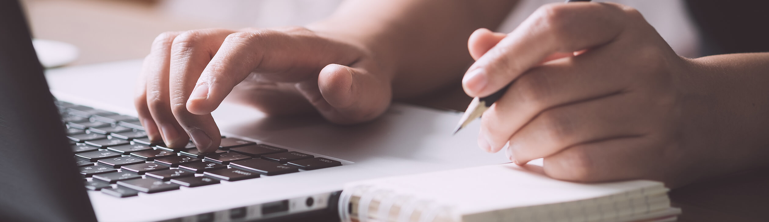 Someone taking notes while working on a laptop